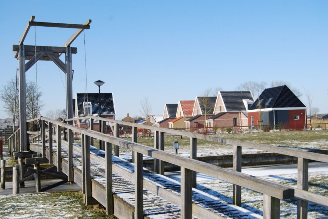 A wooden pedestrian bridge over a canal with houses in the background.