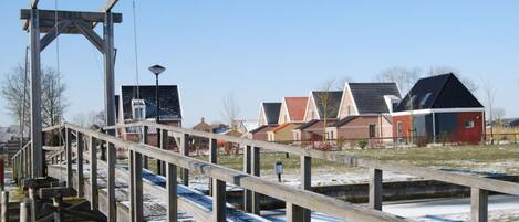 A wooden pedestrian bridge over a canal with houses in the background.