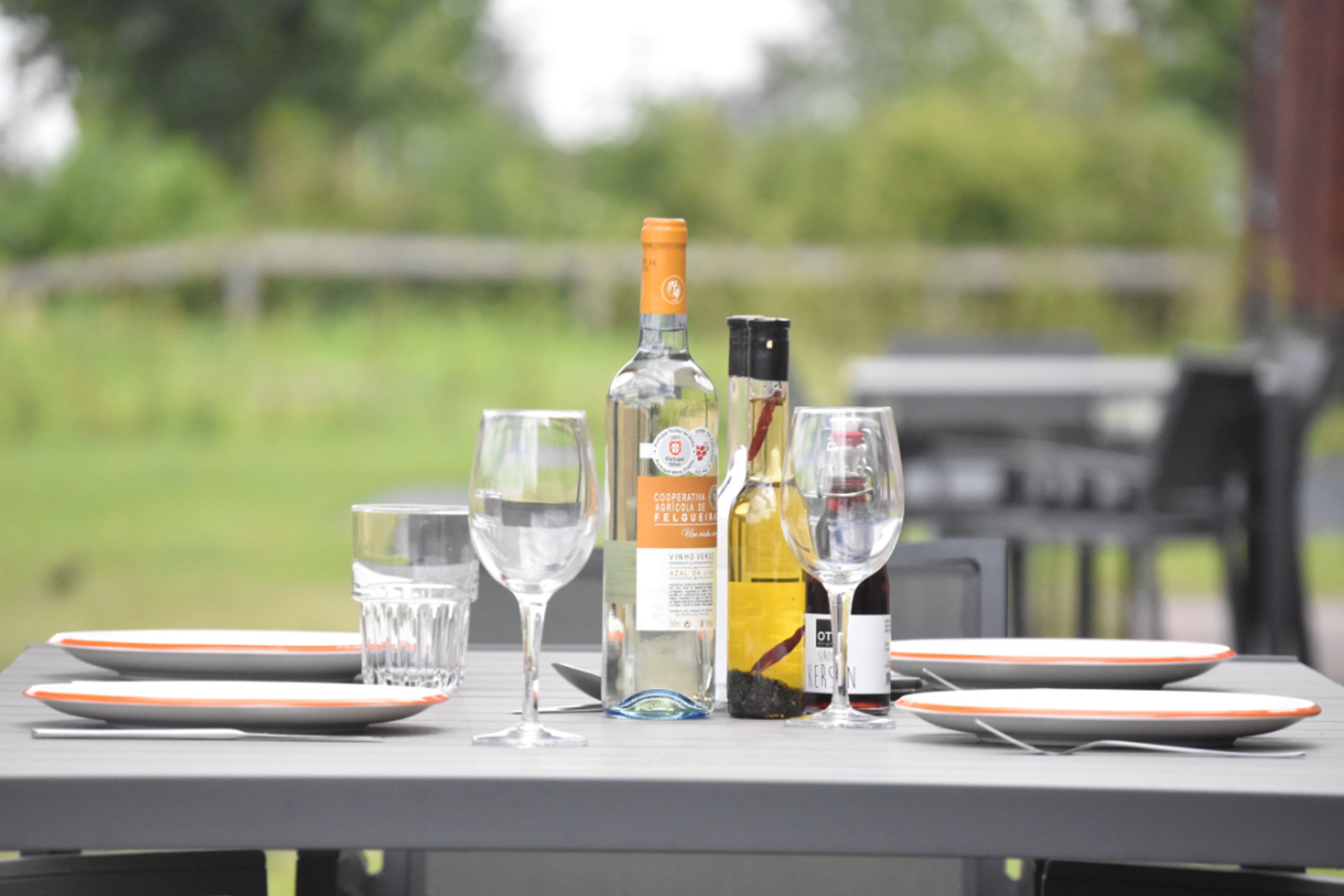 Una mesa dispuesta con copas de vino, platos y botellas, probablemente para una comida o reunión.