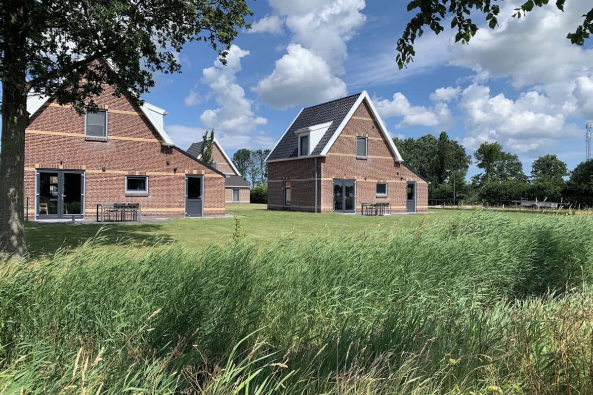 A modern brick building with a sloped roof and large windows, surrounded by a grassy field and trees.