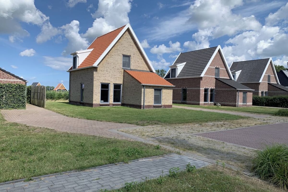 A row of modern houses with pitched roofs and brick exteriors, arranged in a residential neighborhood with paved pathways and green lawns.