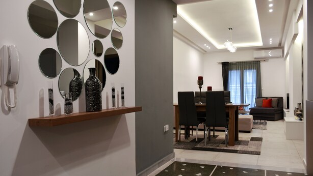 A modern living room with a dining area, a sofa, and a coffee table. There is a mirror wall and a ceiling light fixture.