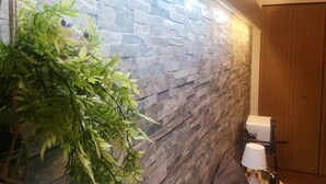 Un baño con pared de piedra, una planta de bambú y un inodoro con tapa blanca.
