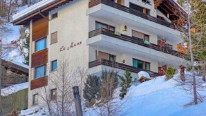 Un edificio a più piani con balconi, immerso nella neve e circondato da alberi.