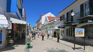 Eine Kopfsteinpflasterstraße gesäumt von Geschäften unter einem wolkenlosen, blauen Himmel.