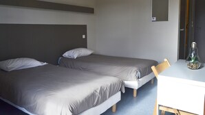 Una habitación con dos camas individuales, una mesita y una silla.