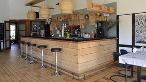 Zona de bar con taburetes de madera, una barra y estantes llenos de botellas y vasos.