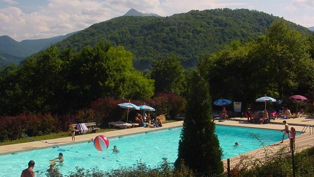 Una piscina con gente, rodeada de exuberante vegetación y montañas al fondo.