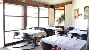 Un restaurante con varias mesas y sillas, ventanas amplias y techo de madera.