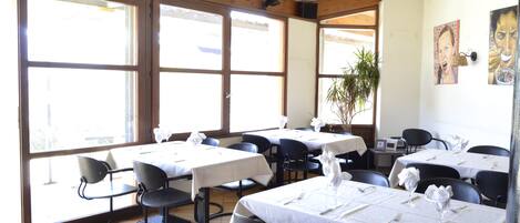 A restaurant with multiple tables and chairs, large windows, and a wooden ceiling.