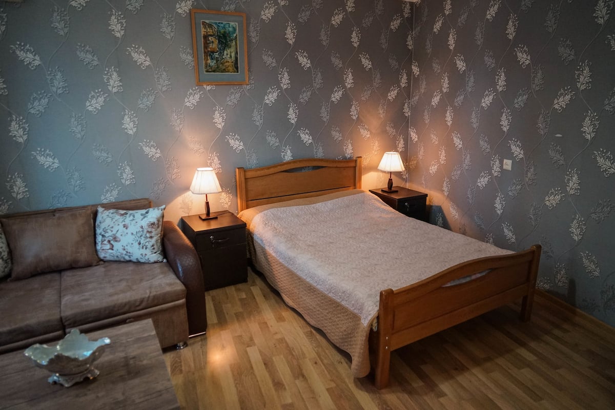 Un dormitorio con una cama de madera, dos mesitas de noche con lámparas, un sofá marrón y una mesa decorativa.