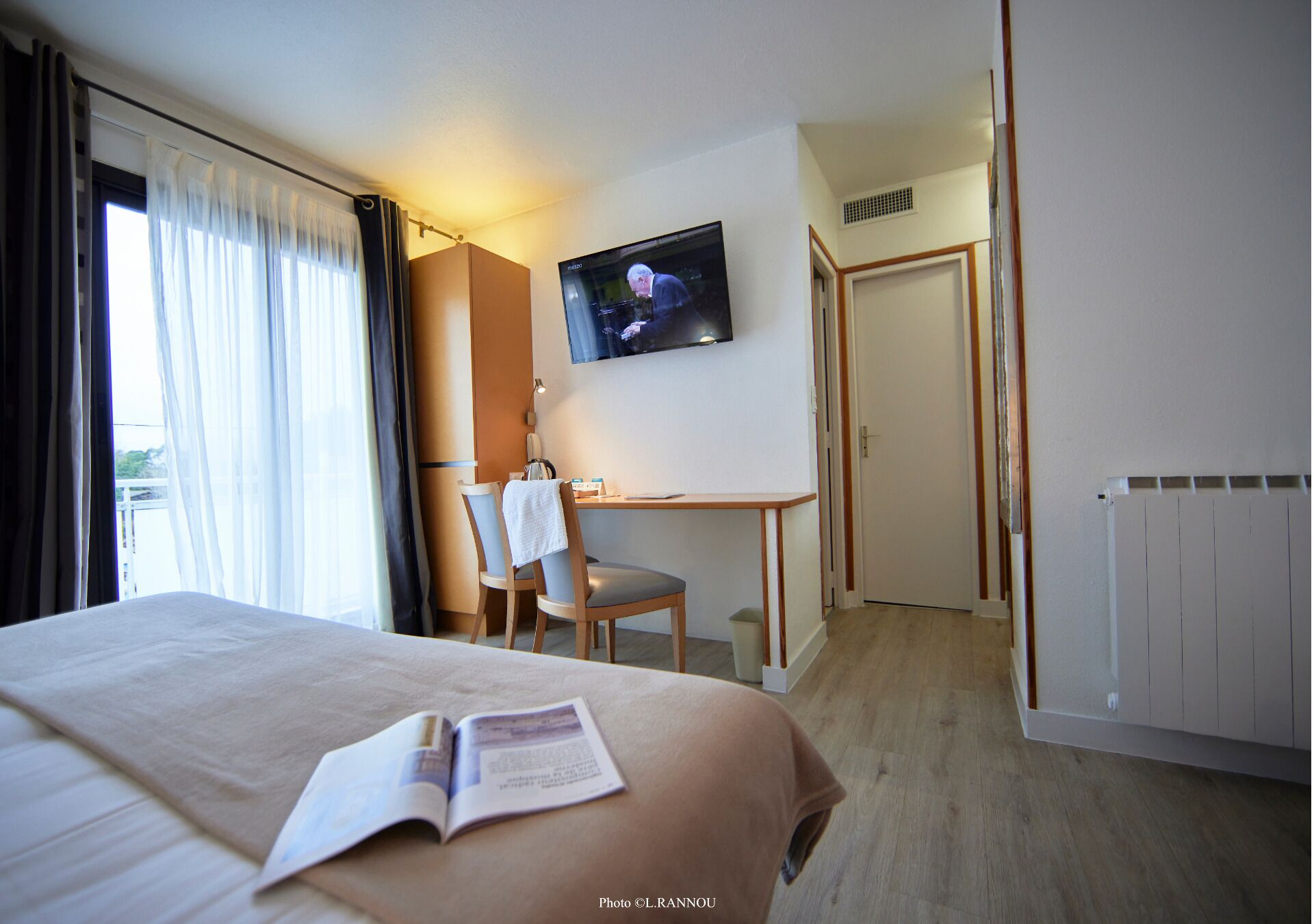 Una habitación de hotel con cama, escritorio, silla, televisor y radiador.