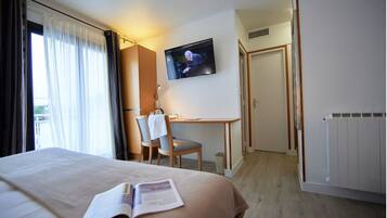 Una habitación de hotel con cama, escritorio, silla, televisor y radiador.