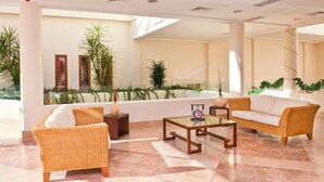 Un hall espacioso con mobiliario de mimbre, una mesa de centro de vidrio y vistas a un jardín ajardinado a través de amplias ventanas.