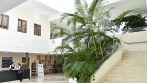Um hall amplo com balcão de recepção, escadaria e plantas verdes em vasos.
