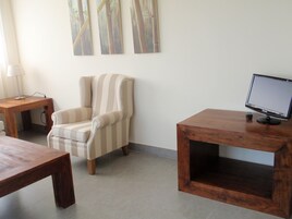 A room with a striped armchair, a wooden table, a TV on a wooden stand, and a lamp on a side table.
