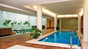 Piscina interna com piso de azulejos, área de recepção com balcão e cadeiras, e plantas em vasos.