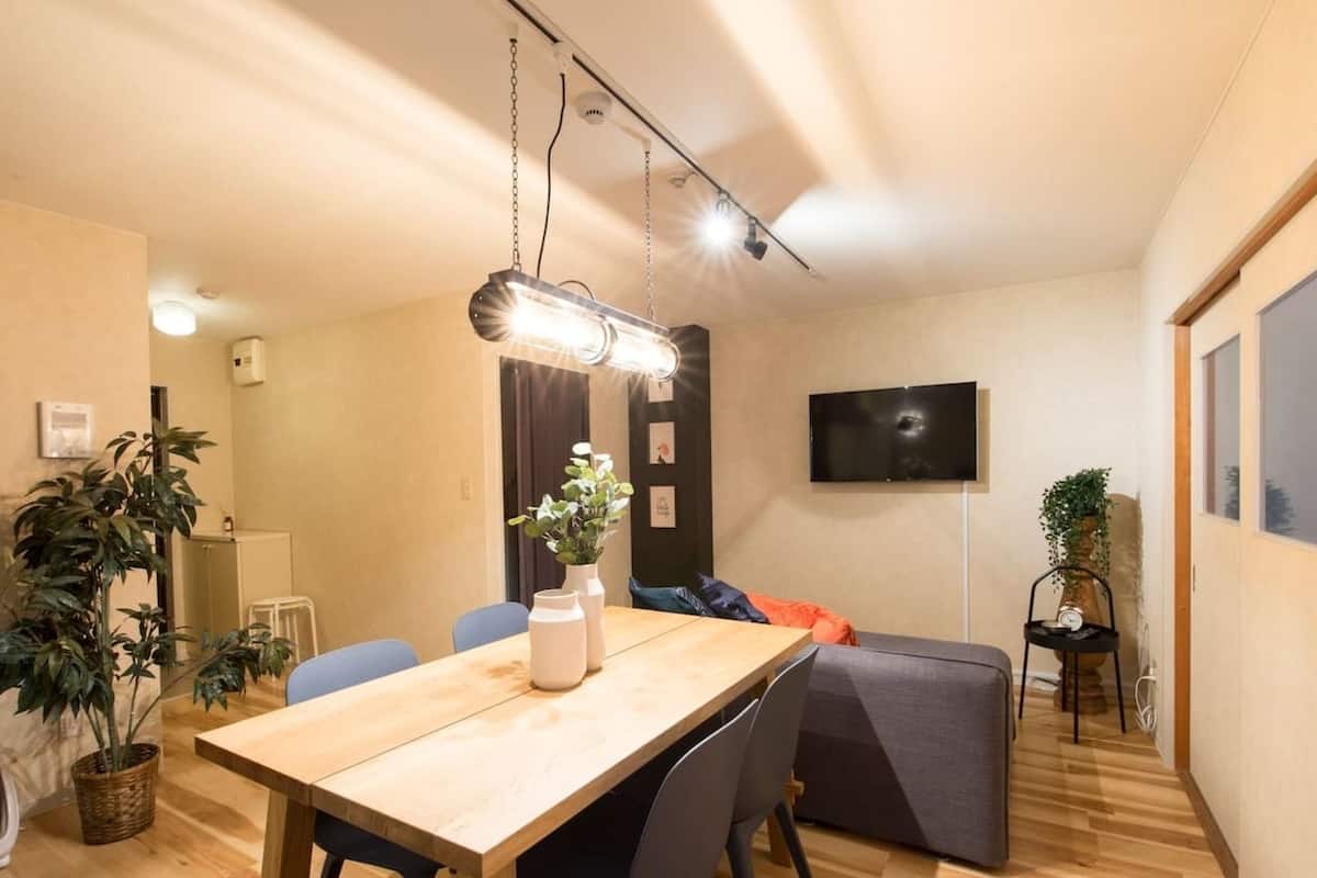 En moderne stue med et træspisebord, blå stole, en grå sofa og et fladskærms-tv monteret på væggen.