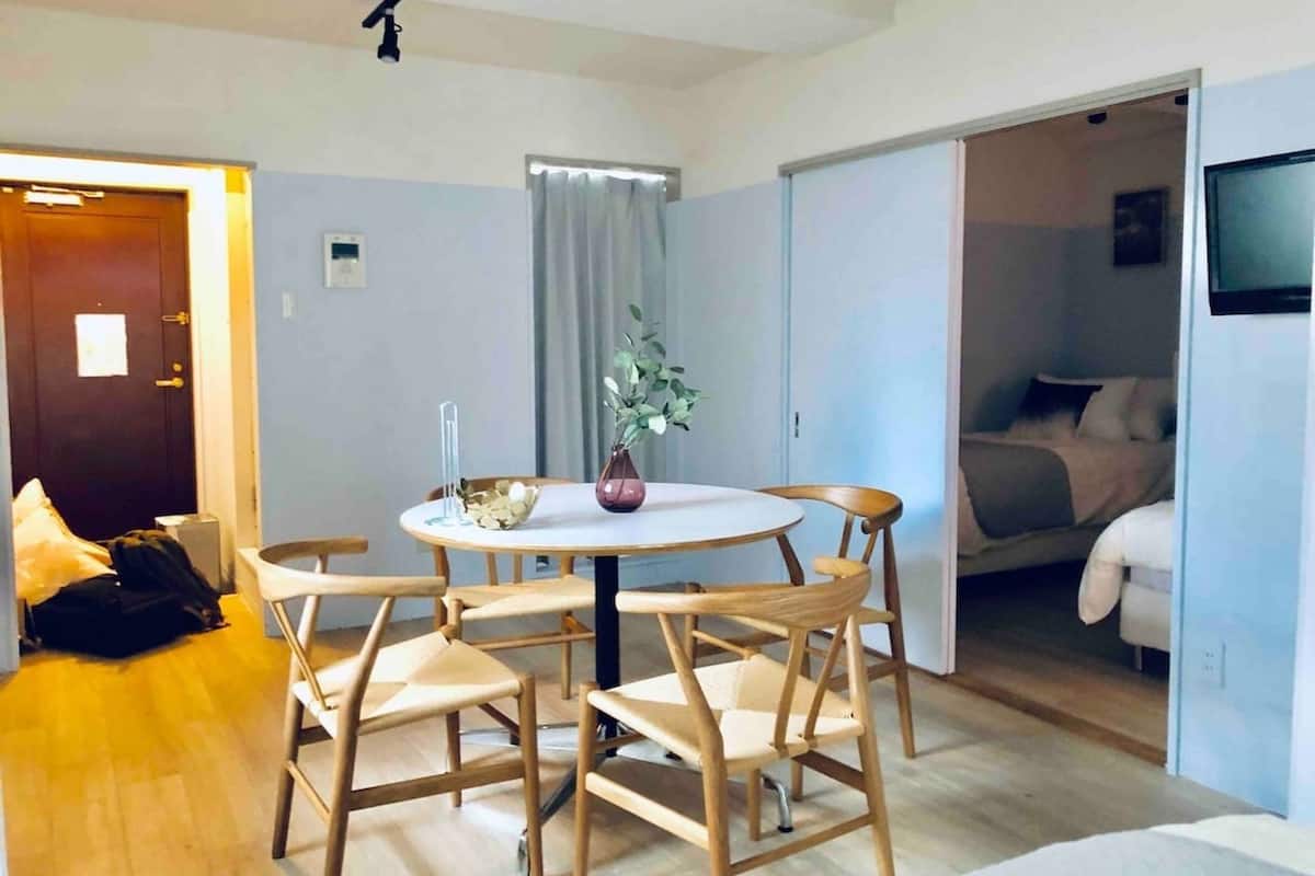 Et lille hotelværelse med et rundt spisebord, fire træstole, en lille potteplante og en seng med hvid dyne.