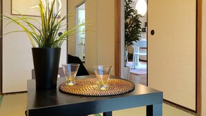 En hall med en krukväxt, två glas på en vävd underlägg och en spegel som reflekterar ett rum med en växt och en vit stol.