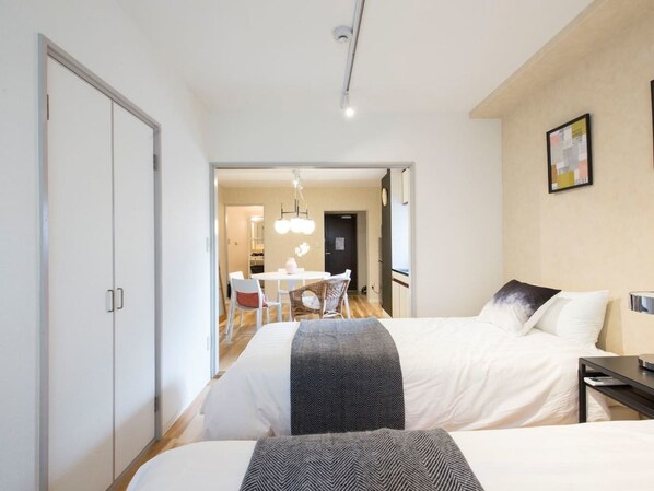 A hotel room with two beds, a dining area, and a hallway.