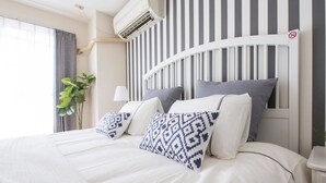Ett hotellrum med en stor säng, ett randigt sänggavel och en krukväxt.