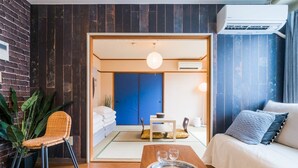 Ett modernt hotellrum med trägolv, en soffa, ett matbord med ett bricka fullt med glas, en blå dörr och en stor växt.