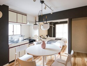 A modern hotel room with a kitchen, a dining area with a round table and chairs, a bed with a view, and a large window.