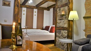 A cozy room with a wooden table, a bed with red pillows, a stone wall, and a lamp.