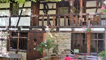A traditional half-timbered building with stone walls, wooden beams, and a balcony with hanging flower baskets.