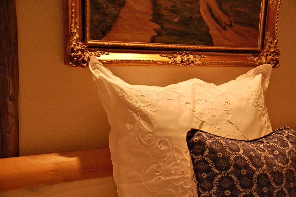Un almohadón blanco con bordado floral y un cojín estampado sobre una cama.