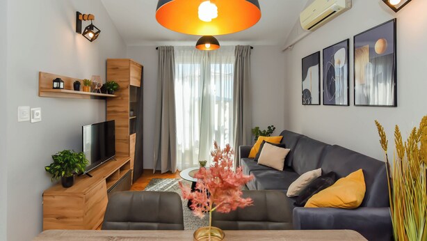 Una sala de estar moderna con un mueble de televisión de madera, un sofá, una mesa de centro con un jarrón y un ventanal con cortinas.