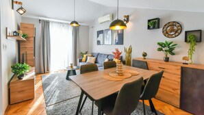 Una sala de estar moderna con comedor, que incluye una mesa de madera, sillas negras, luces colgantes y un sofá con cojines.