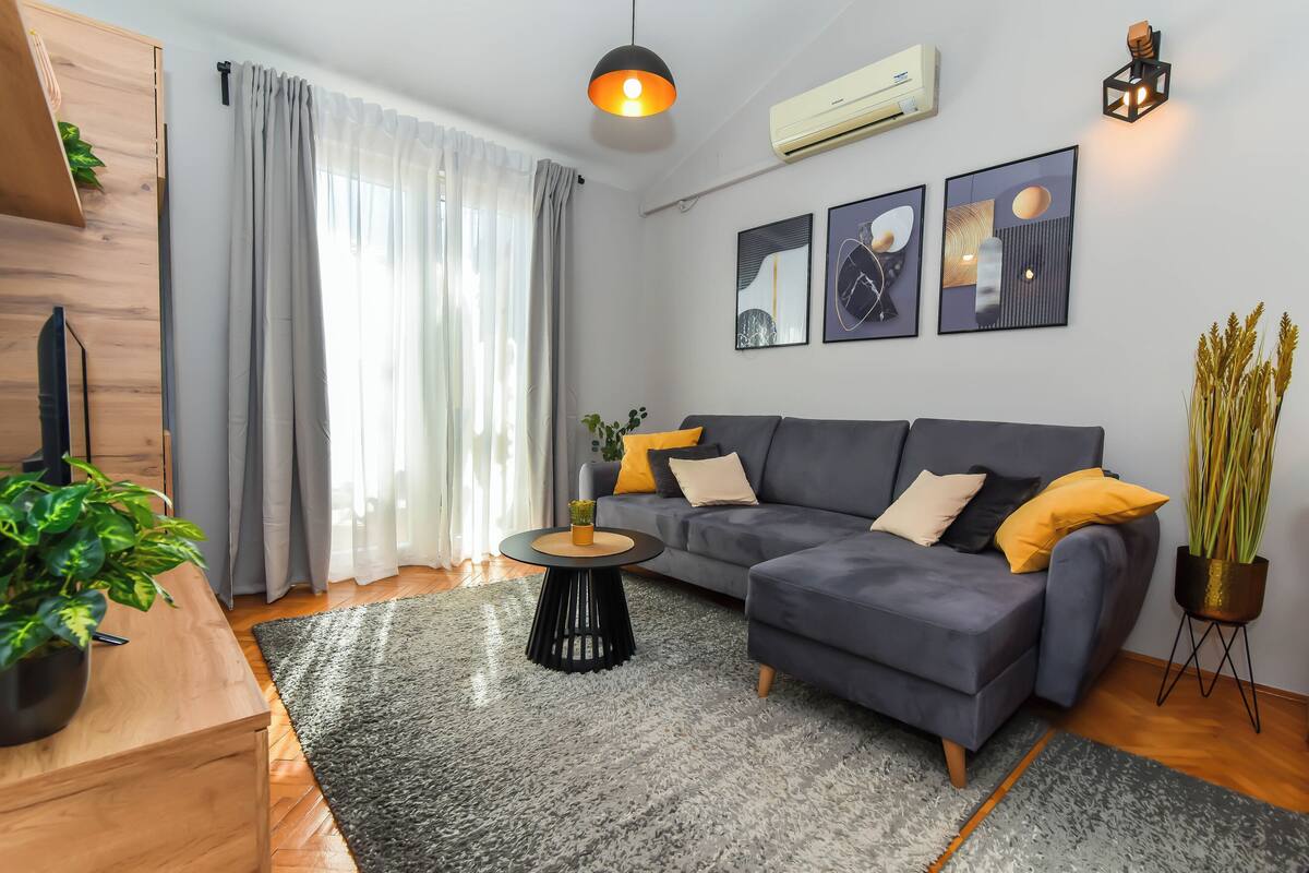 A modern living room with a grey sofa, a round coffee table, and a potted plant.