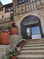 Un edificio de piedra con una escalera de madera que conduce a una puerta de madera oscura. Hay macetas de terracota con flores en los escalones.