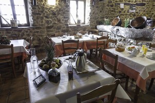 Un comedor rústico con paredes de piedra, mesas y sillas de madera. Hay varios platos y bebidas sobre las mesas.