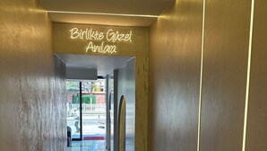 Un couloir moderne, agrémenté d’un panneau néon sur lequel on peut lire « Birlikte Güzel Andina », mène à une porte en verre.