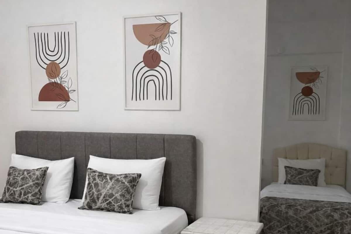 A hotel room with a large bed, a smaller bed, a nightstand, and two abstract wall art pieces.