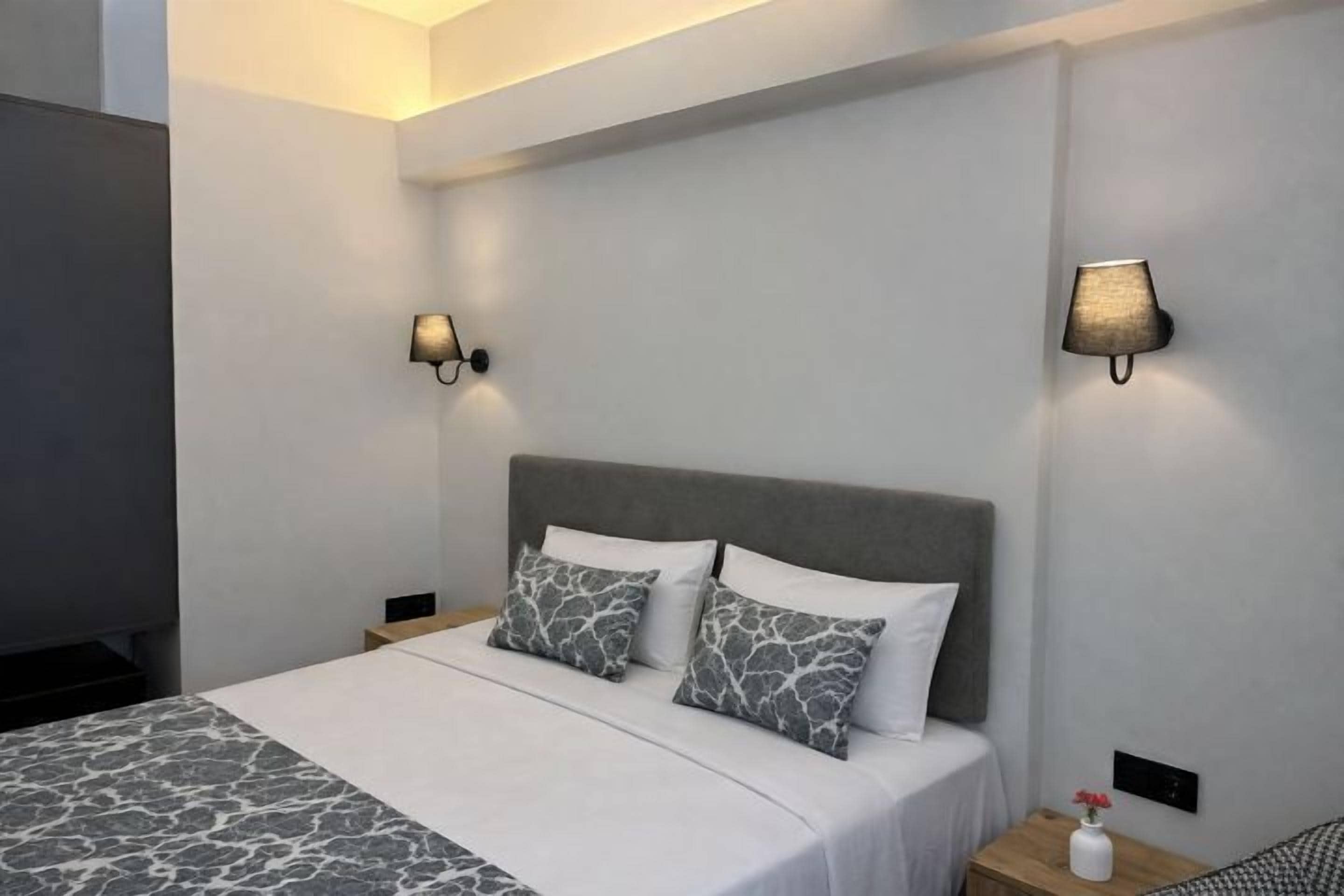 Una habitación de hotel moderna con una cama grande, dos mesitas de noche y lámparas de pared.