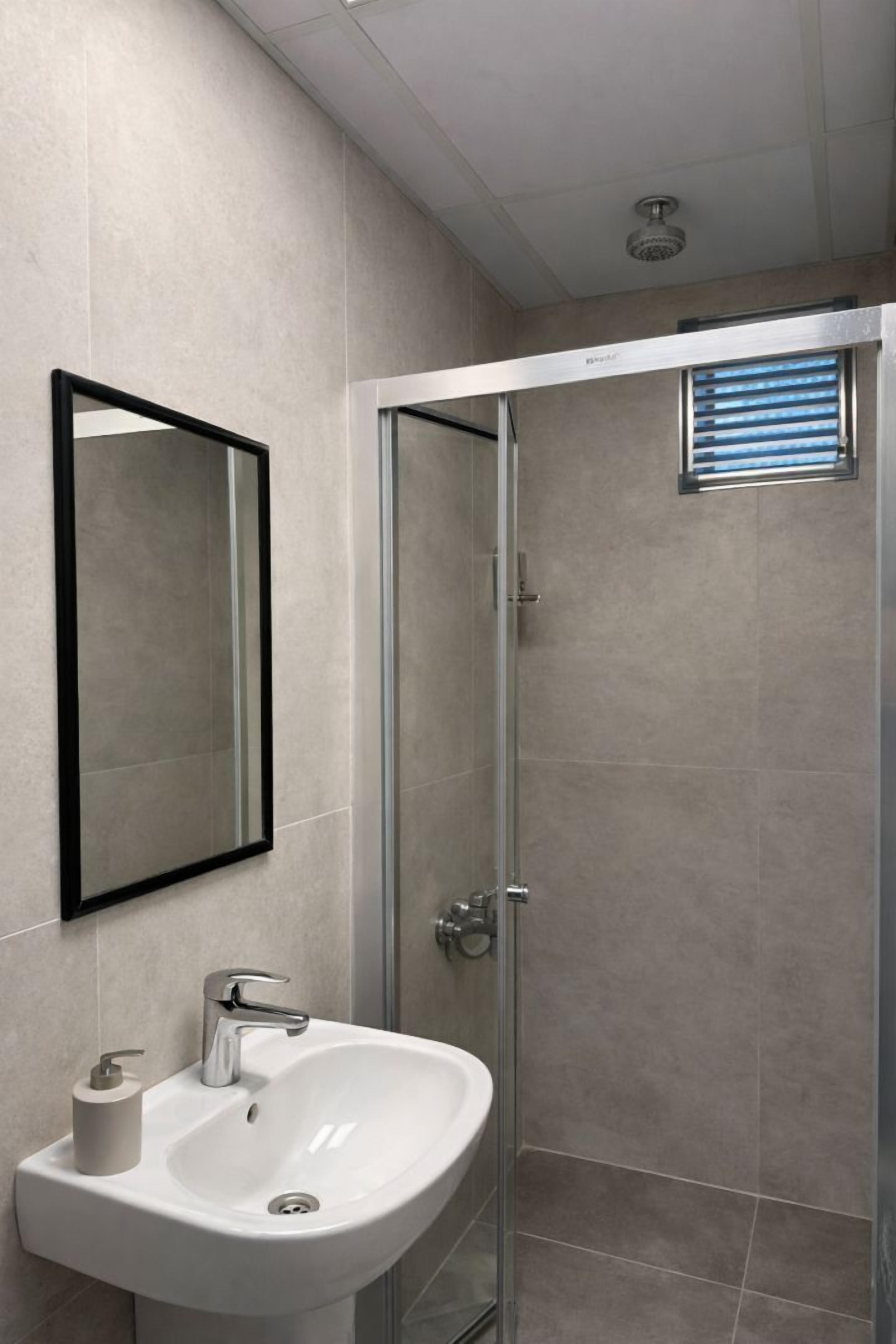 A modern bathroom with a white sink, a mirror, and a glass shower enclosure.