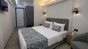 Une chambre d’hôtel moderne dotée d’un grand lit, de deux tables de chevet, d’un téléviseur à écran plat et de lampes fixées au mur.