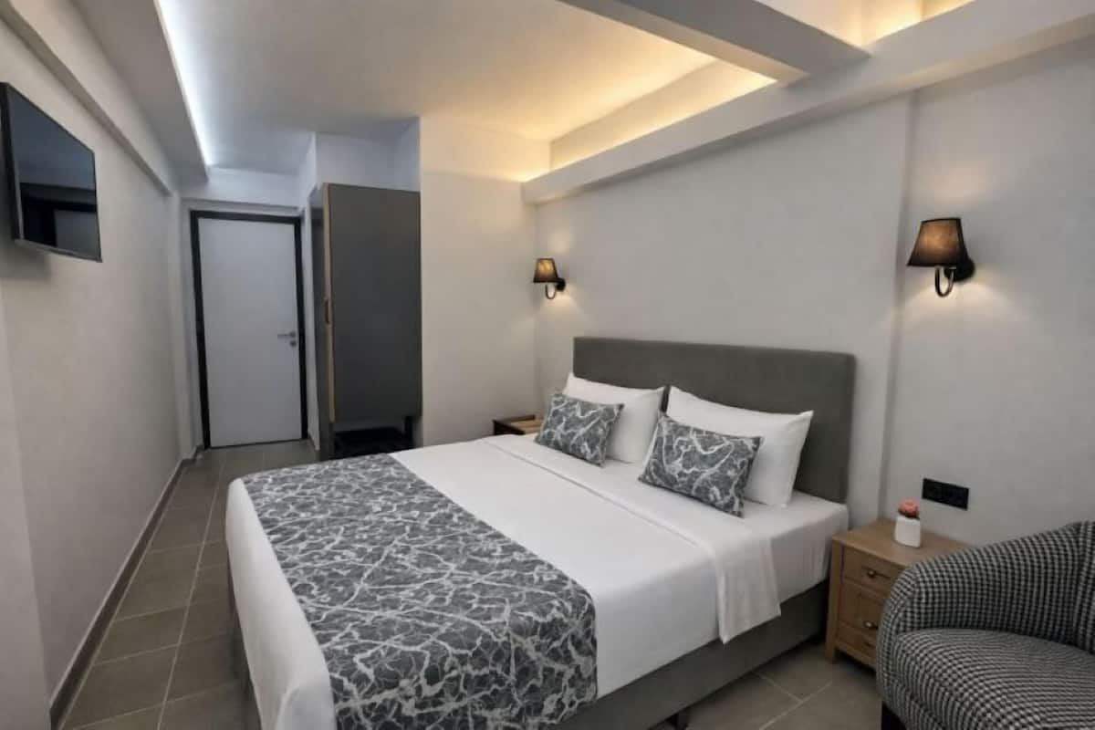 A modern hotel room with a large bed, two bedside tables, a flat-screen TV, and wall-mounted lamps.