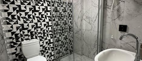 A modern bathroom with a geometric-patterned wall, a glass-enclosed shower, a white toilet, and a sink with a mirror.