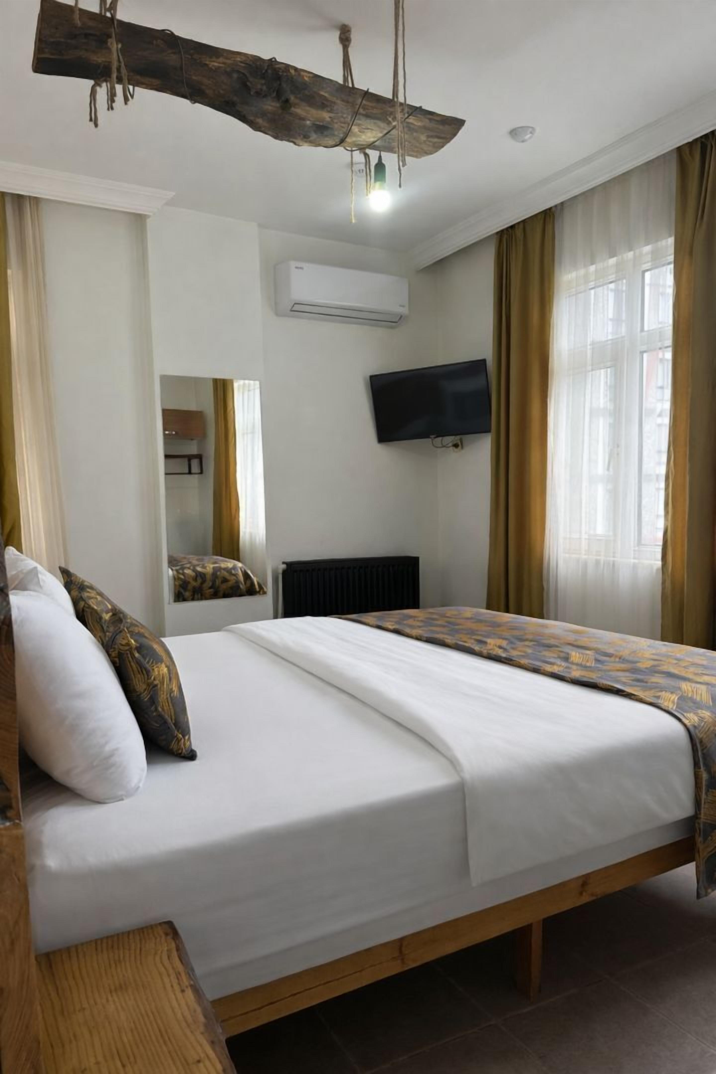 A hotel room with a large bed, a mounted TV, an air conditioning unit, and a window with curtains.
