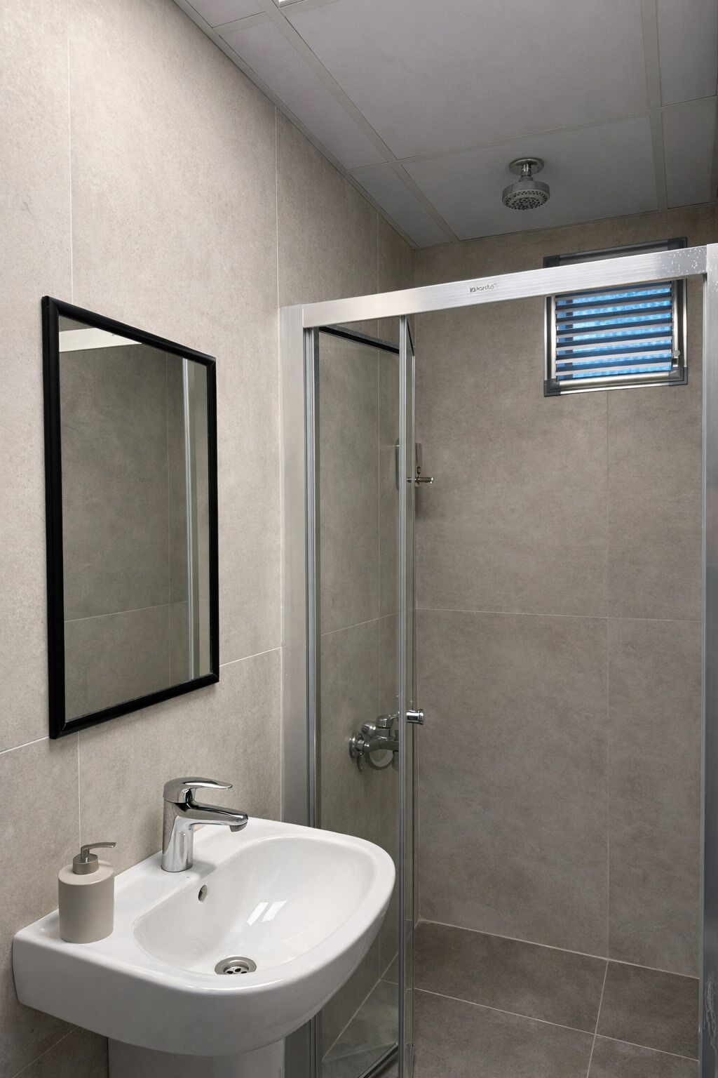 A bathroom with a glass-enclosed shower, a white sink with a soap dispenser, and a mirror on the wall.