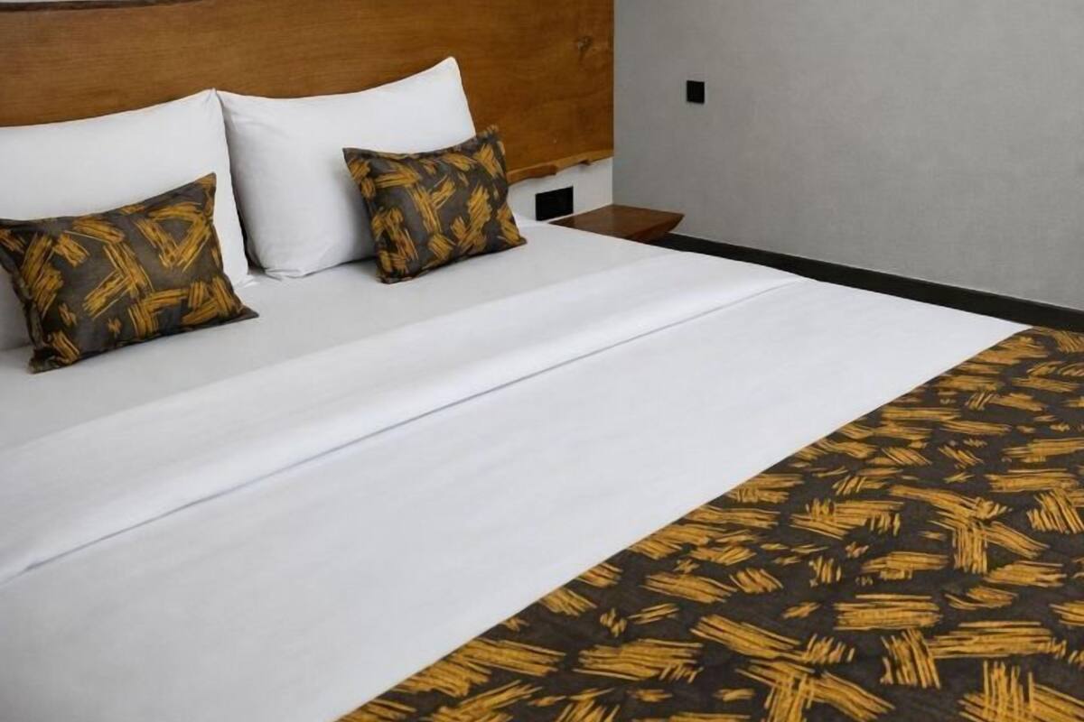 A hotel room with a large bed, a wooden headboard, and a patterned throw blanket.