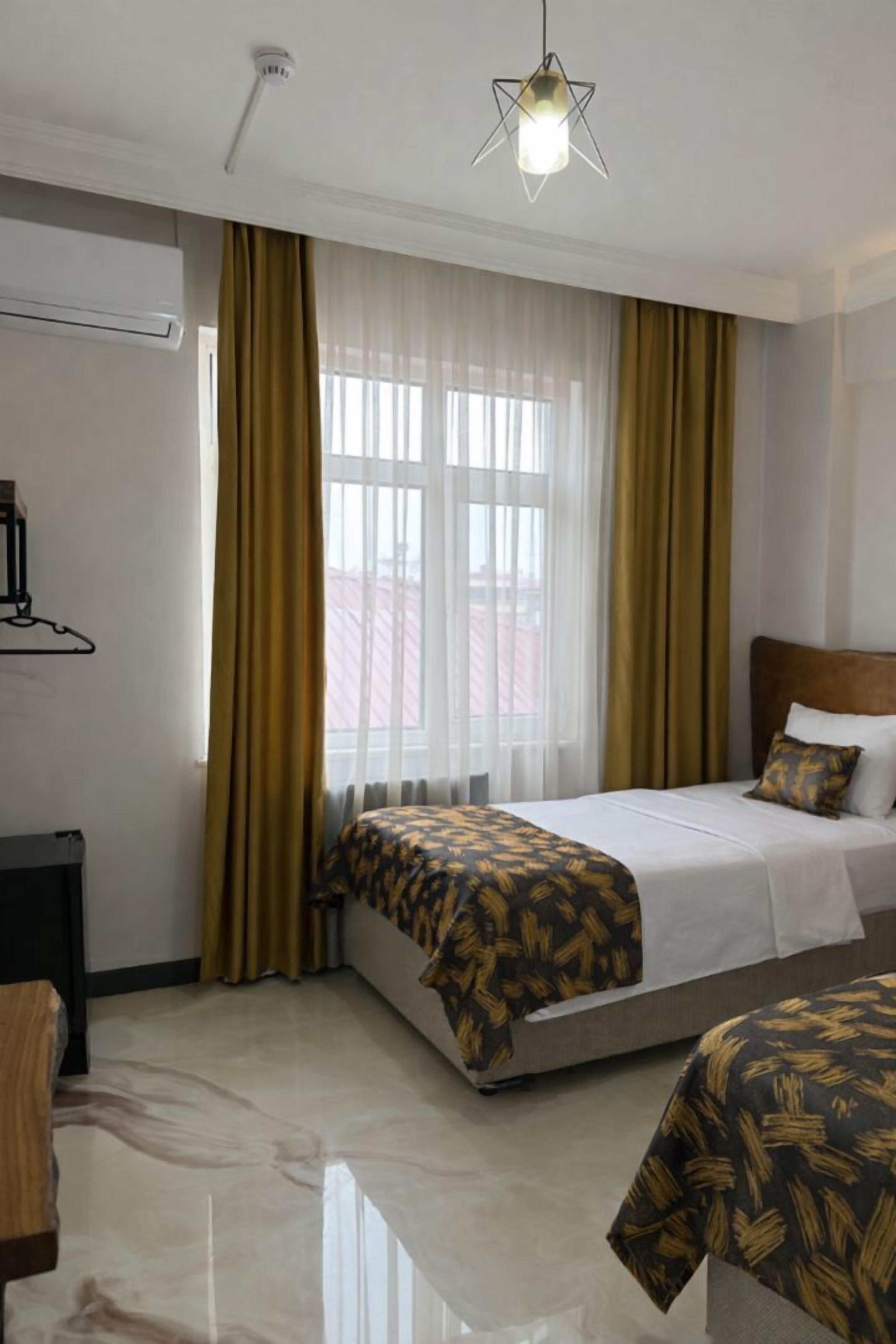 A hotel room with a bed, a bedside table, a hanging light fixture, and a window with curtains.