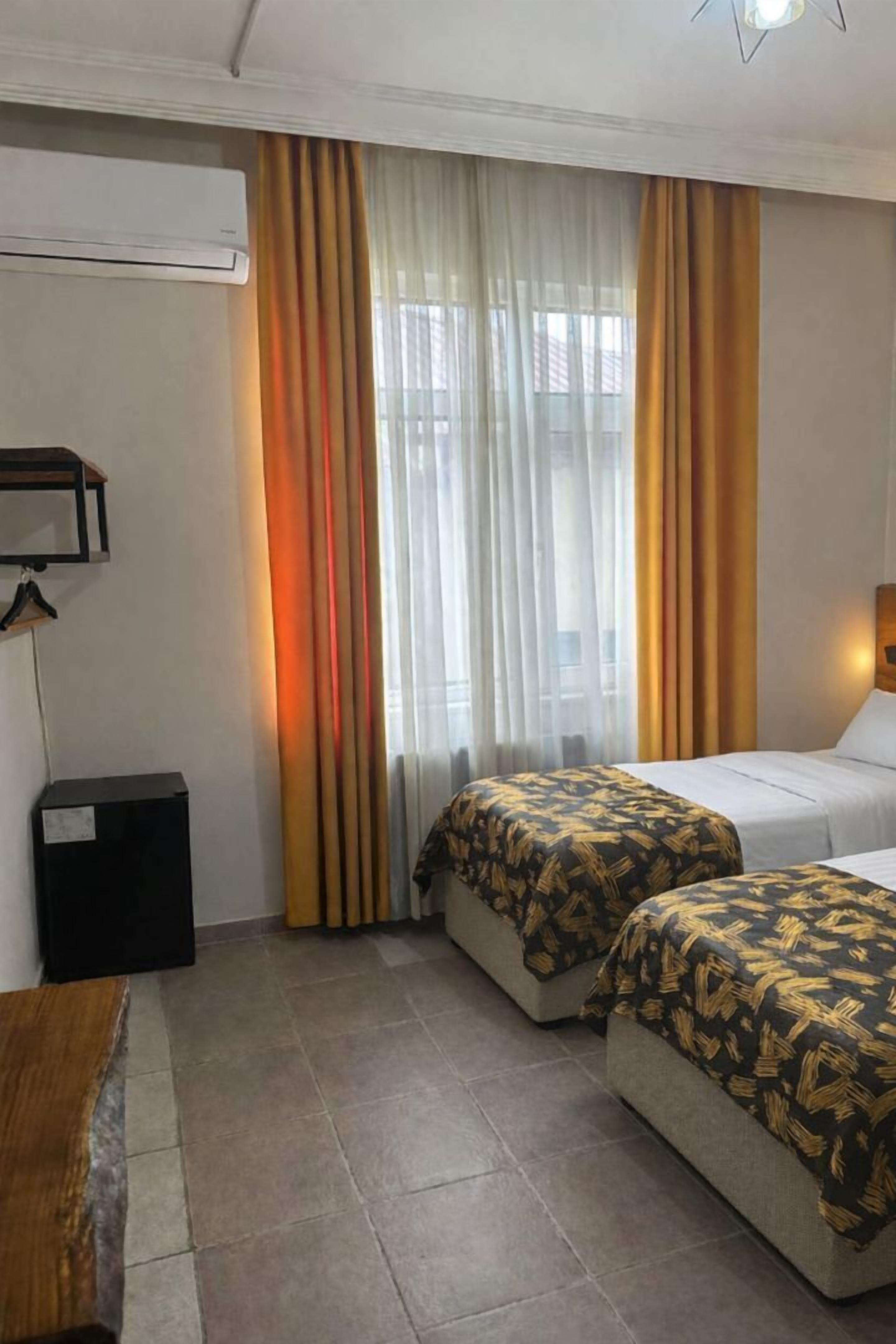A hotel room with two beds, a wooden table, an air conditioner, and a window with curtains.