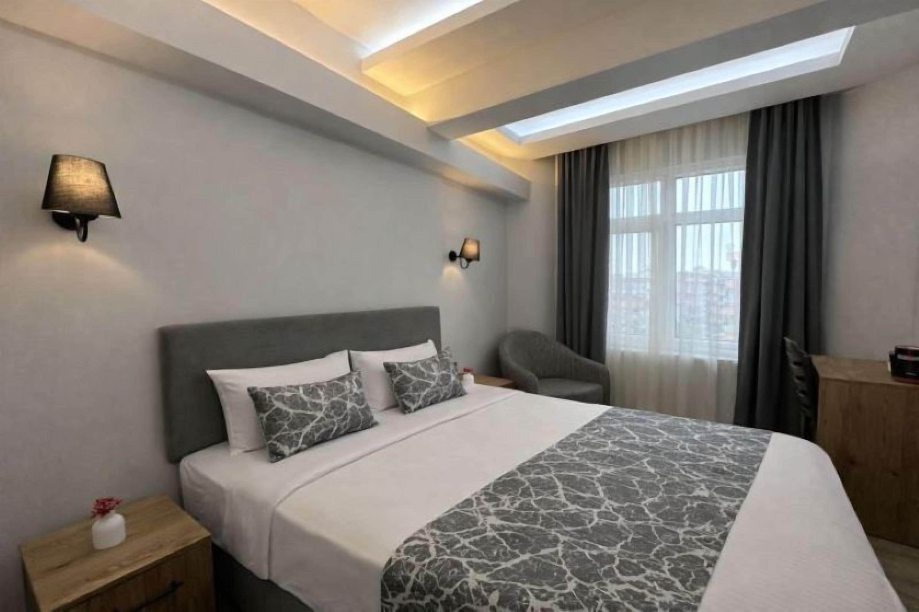 A modern hotel room with a large bed, two wall-mounted lamps, a desk, and a chair.