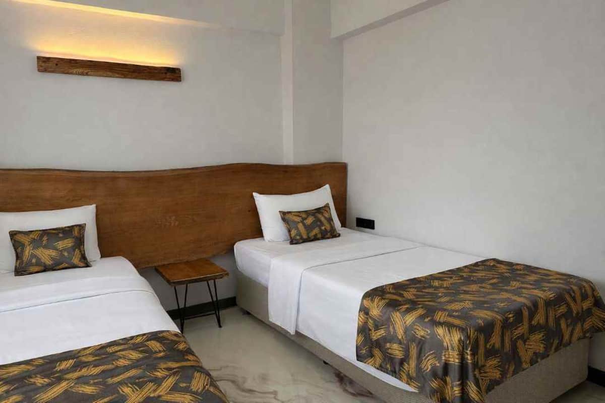 A hotel room with two single beds, each with a wooden headboard and white bedding. There is a small wooden nightstand between the beds.